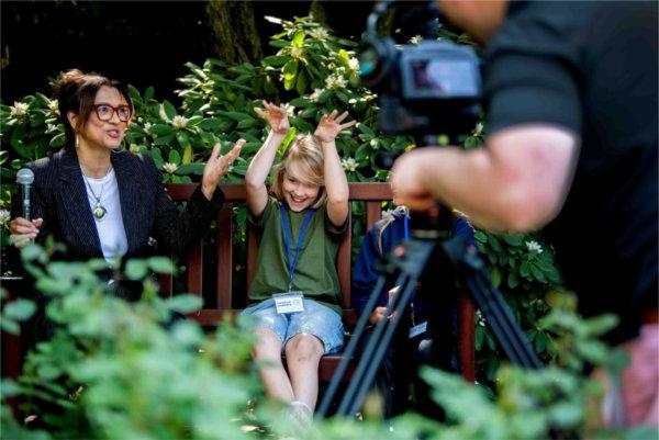  An elementary school student tosses their hands in the air and laughs while being interviewed. 